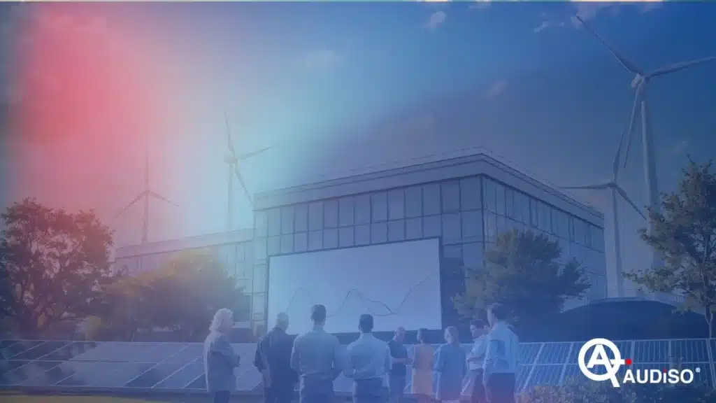 La gente sta all'esterno a guardare un grande schermo che mostra grafici, con turbine eoliche e pannelli solari nelle vicinanze e un edificio moderno sullo sfondo.