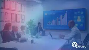 Un gruppo di persone in una sala conferenze sta guardando una presentazione su un grande schermo che mostra grafici e diagrammi. Sono visibili computer portatili e certificati.