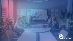 Sei persone in una sala riunioni discutono di dati visualizzati su un grande schermo. Sul tavolo ci sono computer portatili e fogli con grafici.